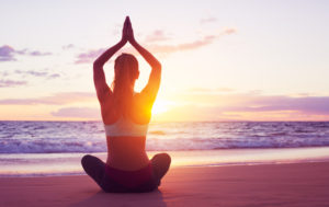 Young healthy woman practicing yoga on the beach at sunset